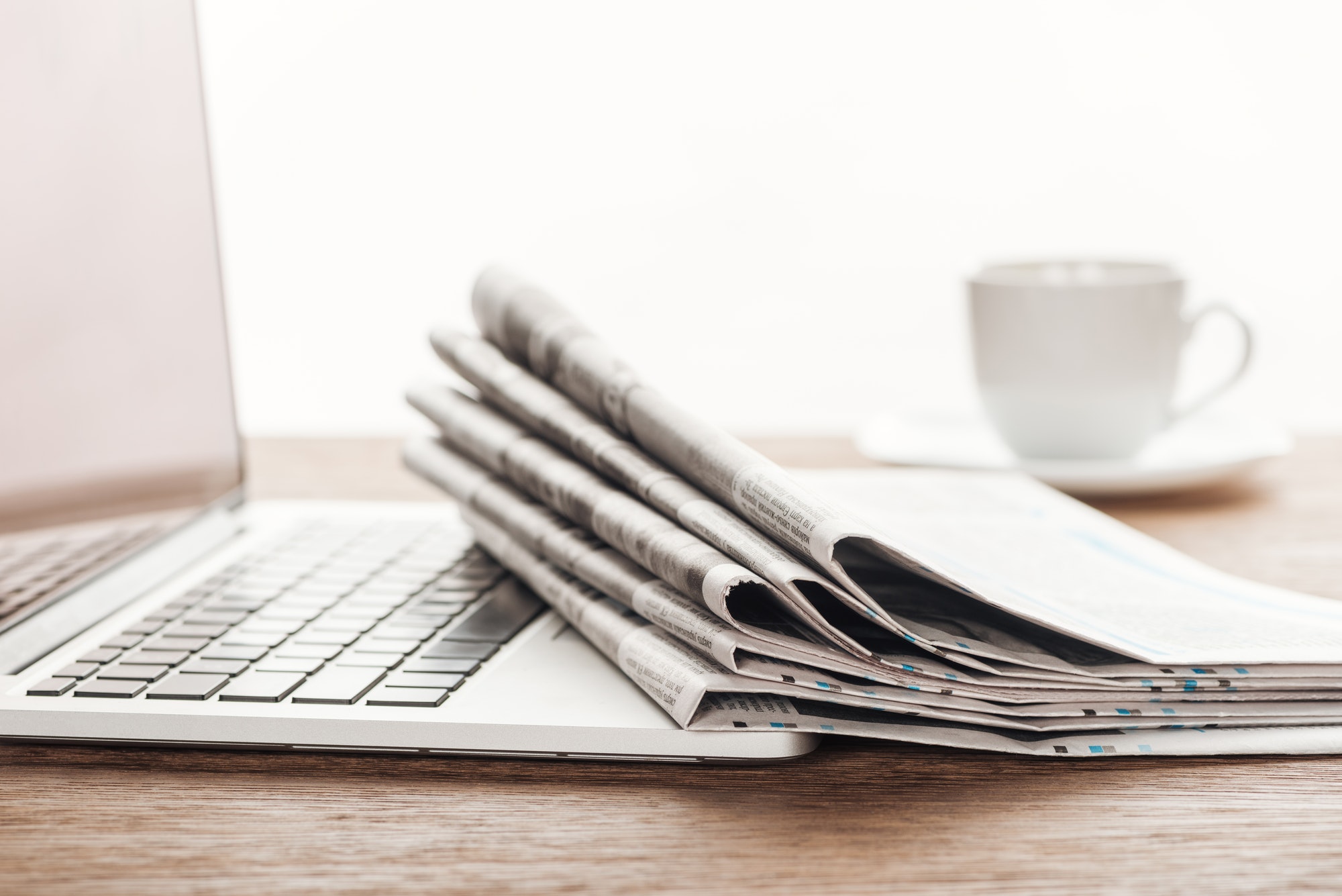 laptop, cup of coffee and stack of newspapers on wooden tabletop
